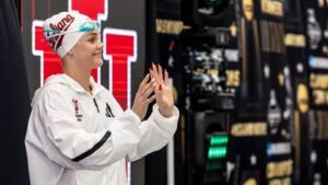 An Indiana University swimmer wearing a swim cap and white jacket clapping at a collegiate swimming