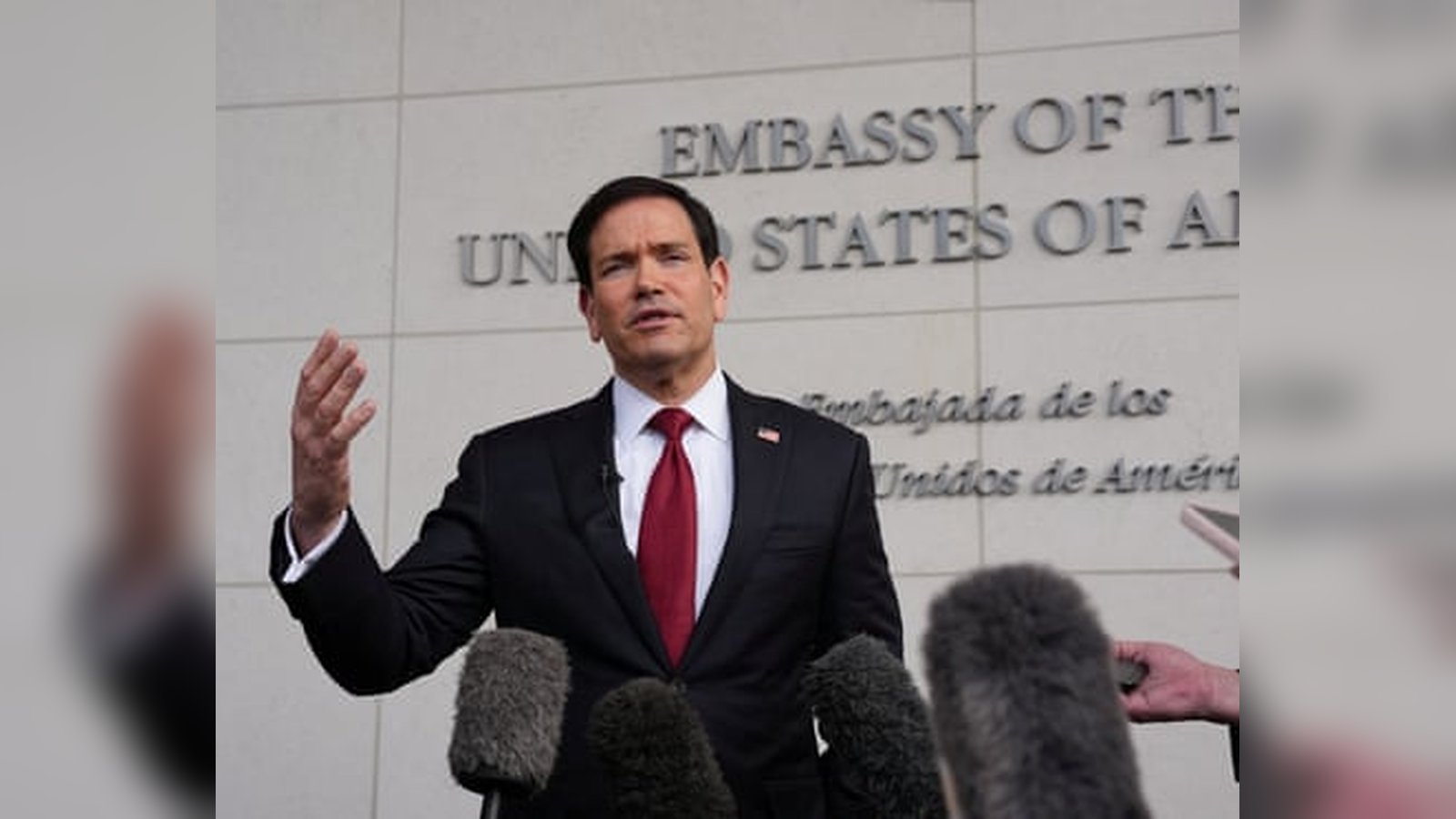 Marco Rubio speaking at a podium in front of the US Embassy building