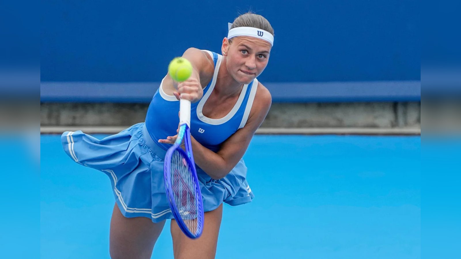 Marta Kostyuk in a blue tennis outfit serving a ball on a court