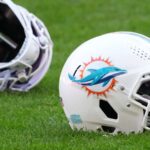 Two Miami Dolphins football helmets resting on the green grass of a stadium field