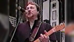Neil Henderson playing guitar and singing into a microphone during a live performance