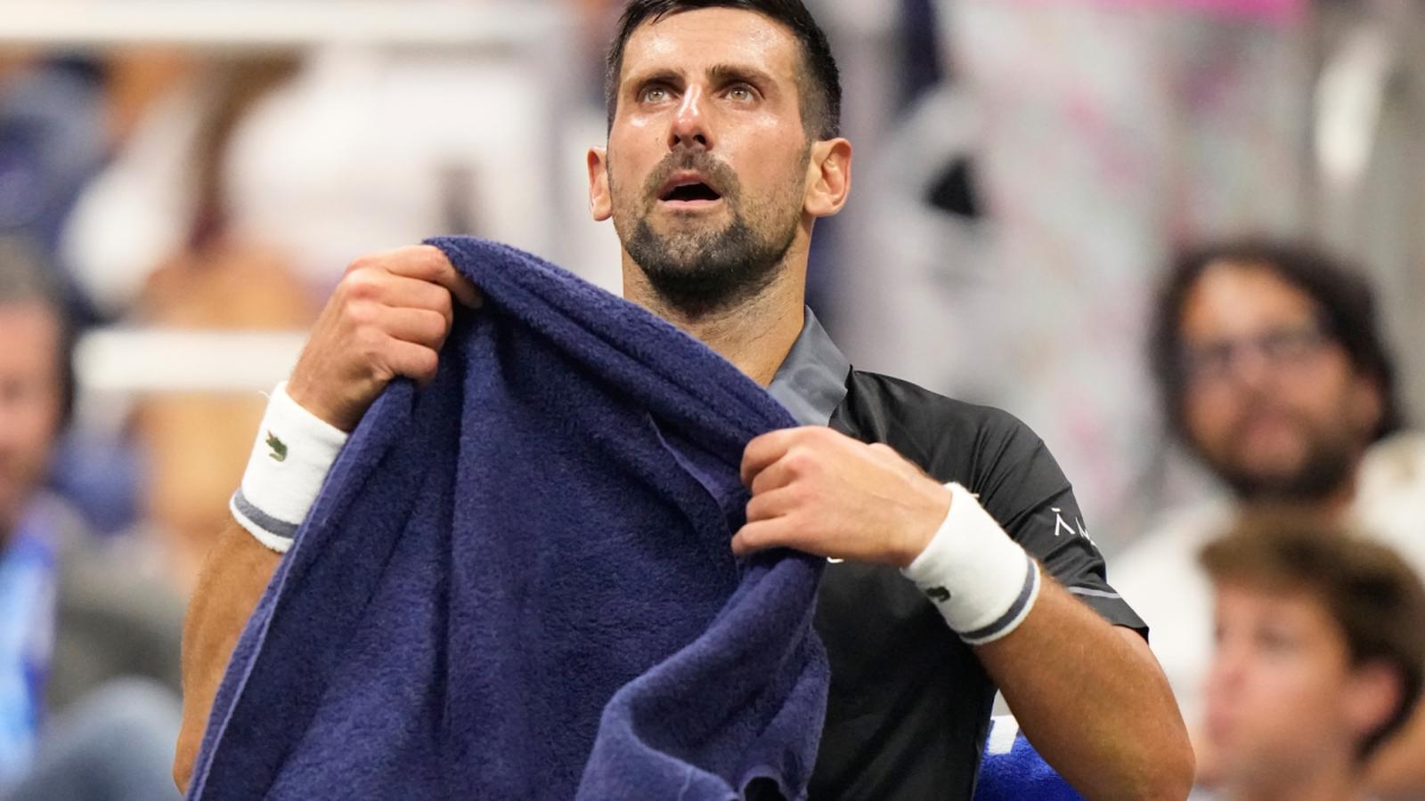 Novak Djokovic looking up while holding a blue towel during a tennis match