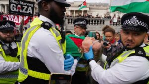 British police officers detaining a protester during a demonstration in London with Palestine flags
