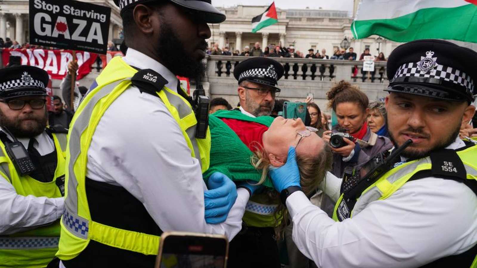 British police officers detaining a protester during a demonstration in London with Palestine flags