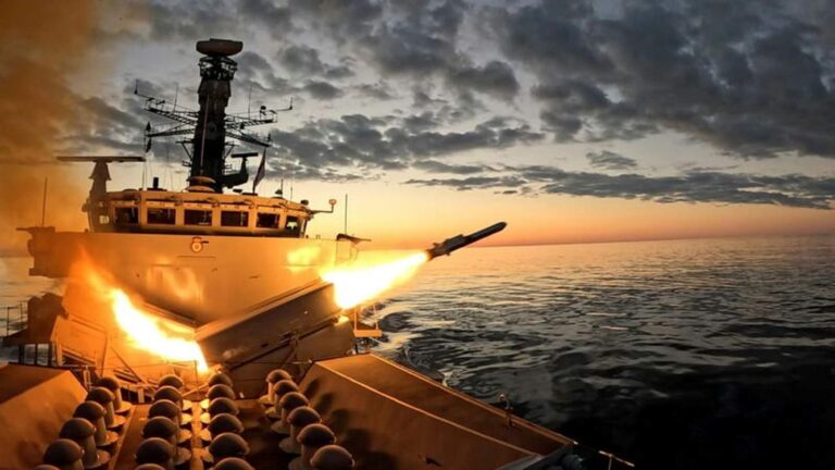 A Royal Navy warship launching a guided missile over the sea at sunset