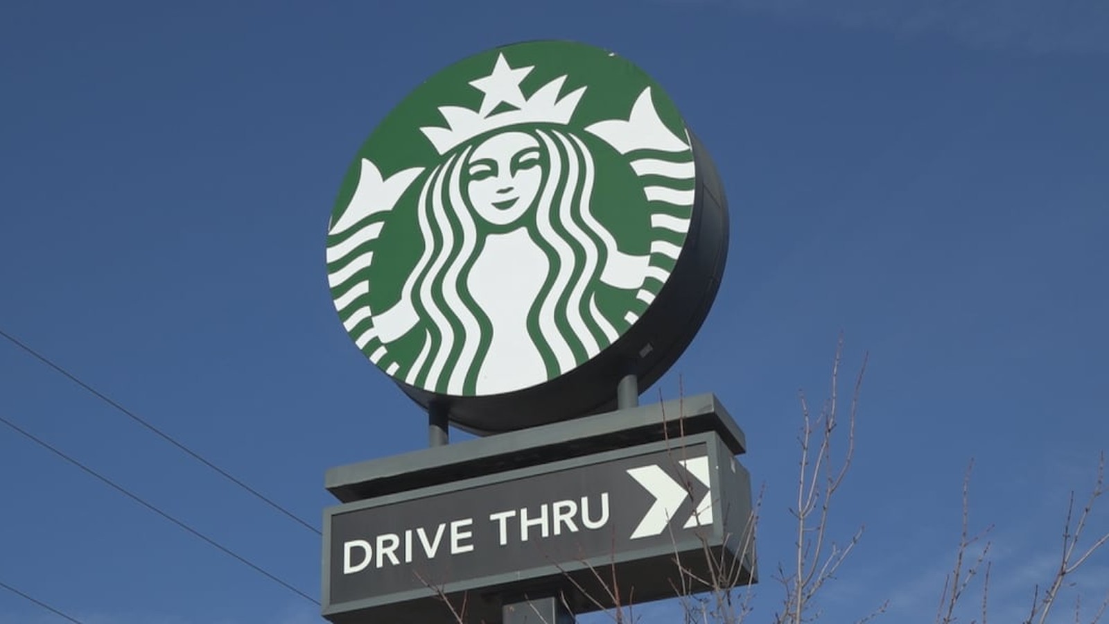 A circular green Starbucks logo sign mounted above a drive thru directional sign