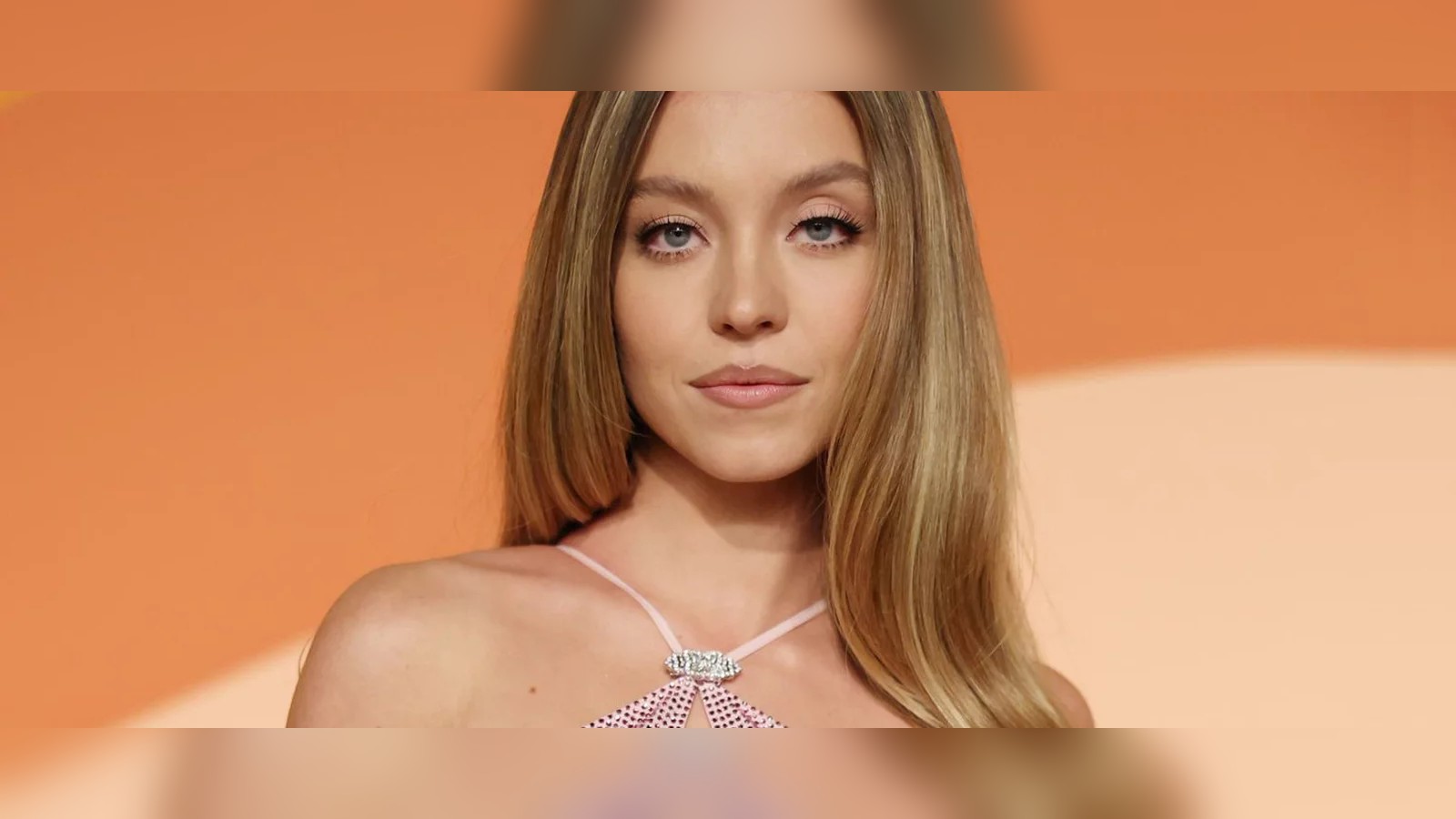 Actress Sydney Sweeney posing against an orange background for a promotional event