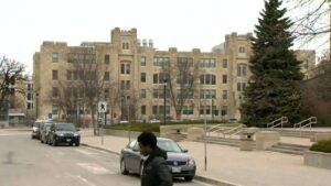 The historic stone building of the University of Manitoba campus with cars parked nearby