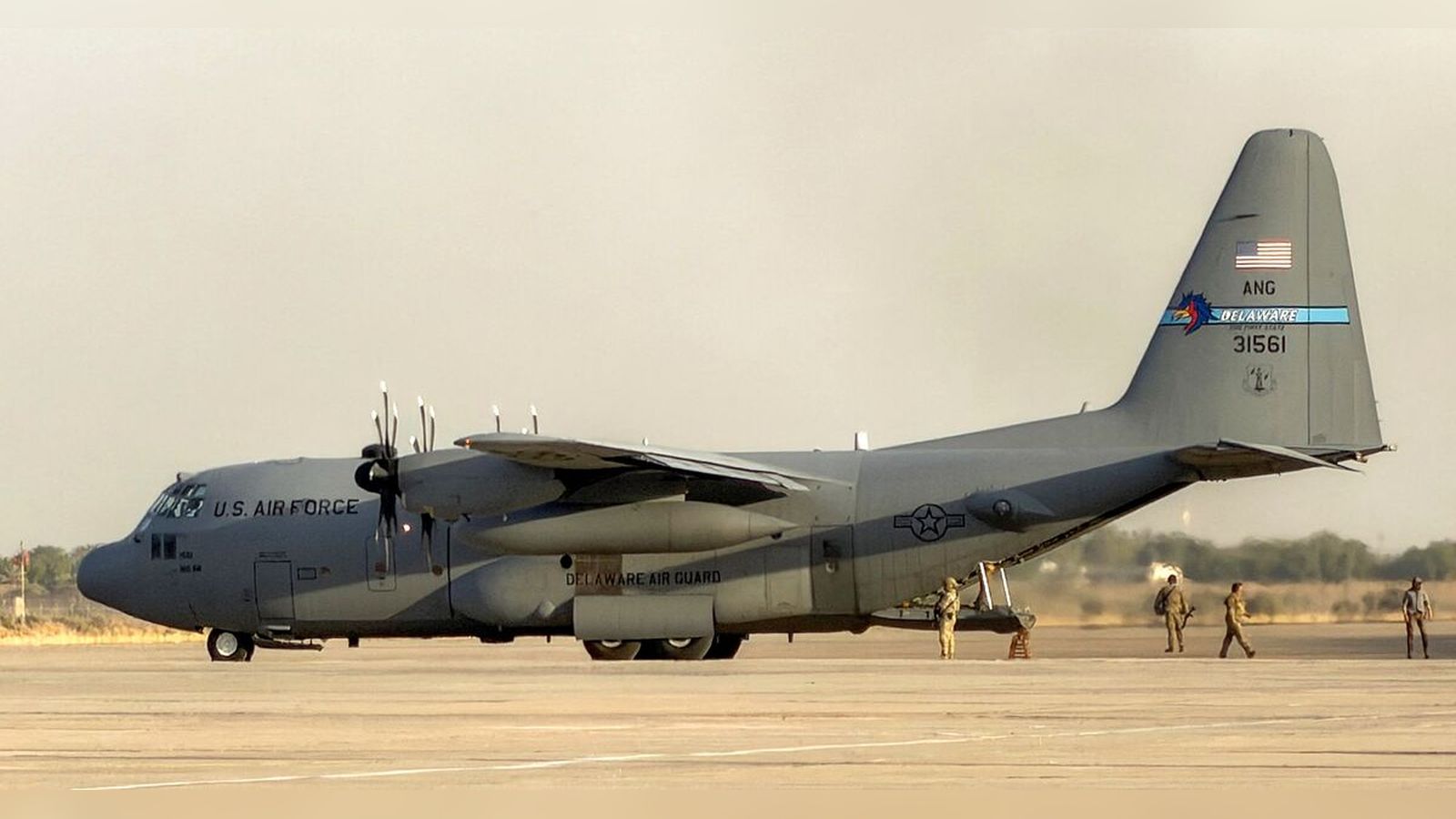 A US Air Force C-130 transport aircraft parked on an airfield with personnel nearby