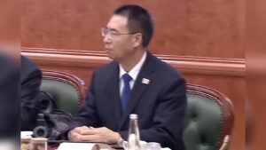 Zhou Hongxu wearing a suit and glasses seated at a conference table