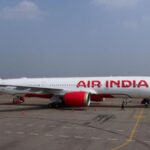 An Air India commercial airplane parked on an airport tarmac with ground staff nearby