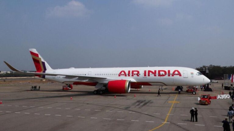 An Air India commercial airplane parked on an airport tarmac with ground staff nearby