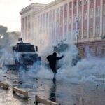 A protester amidst smoke and police vehicles during demonstrations in front of government buildings
