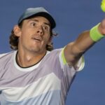 Alex de Minaur tossing a tennis ball to serve during a match on hard court