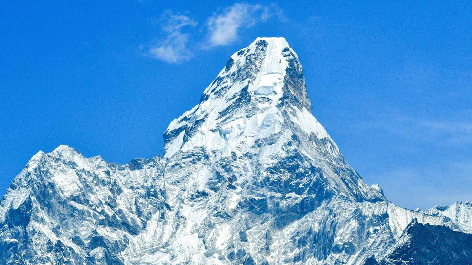 Snow-covered peak and ridge of Ama Dablam mountain against a bright blue sky