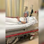 Young woman wearing a surgical cap and hospital gown waving from a stretcher bed