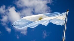 The national flag of Argentina waving on a flagpole against a blue sky with clouds