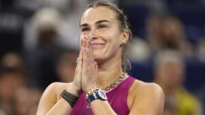 Aryna Sabalenka smiling and holding hands together in gratitude on the court