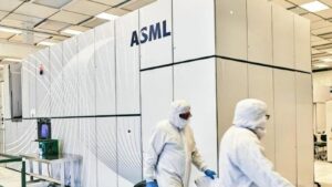 Workers in white cleanroom suits walking past a large ASML semiconductor manufacturing machine