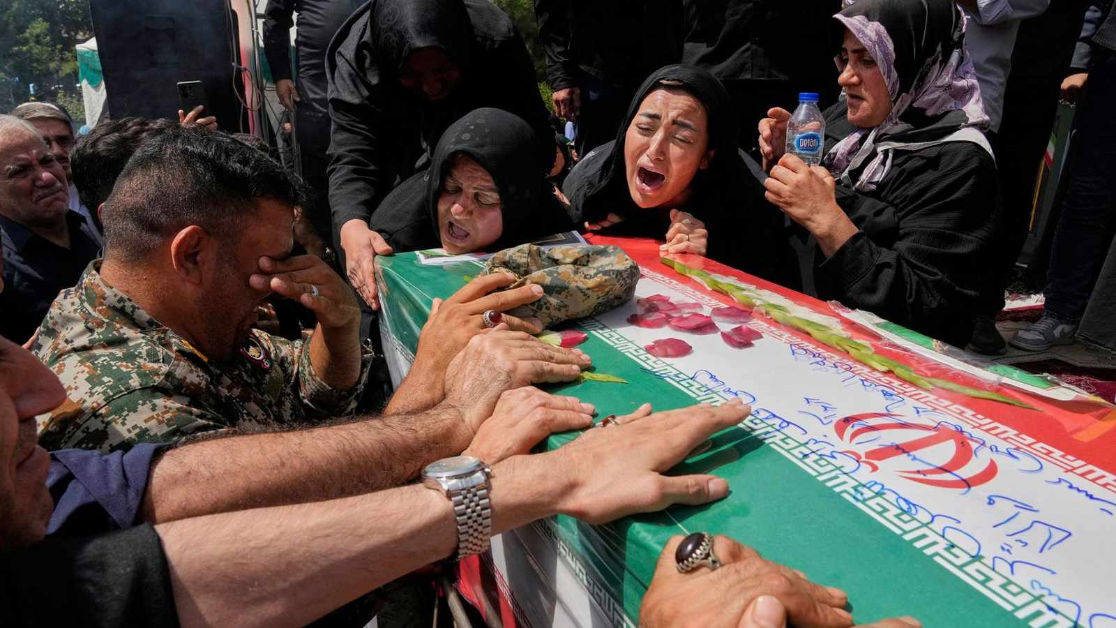 Mourners grieving over a casket draped with the Iranian flag during a funeral service