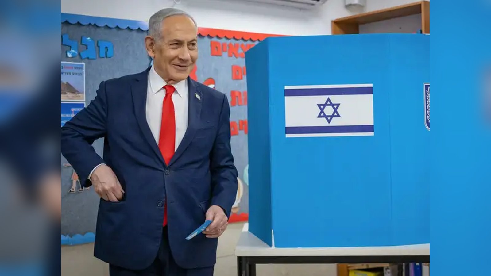 Prime Minister Benjamin Netanyahu smiling while holding a ballot near a voting booth in Israel