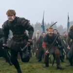 Group of Viking warriors in historical armor charging across a misty field with swords