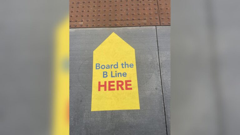 Yellow arrow sign on concrete sidewalk pointing the way to board public transit