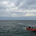 An orange and white rescue boat navigates choppy ocean waters under a cloudy sky