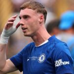 Cole Palmer wearing a blue Chelsea football kit with hand raised to his head