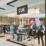 A Cue clothing boutique storefront displaying mannequins in a modern shopping center