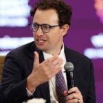 Anthropic CEO Dario Amodei wearing glasses and suit gesturing while speaking at a conference panel