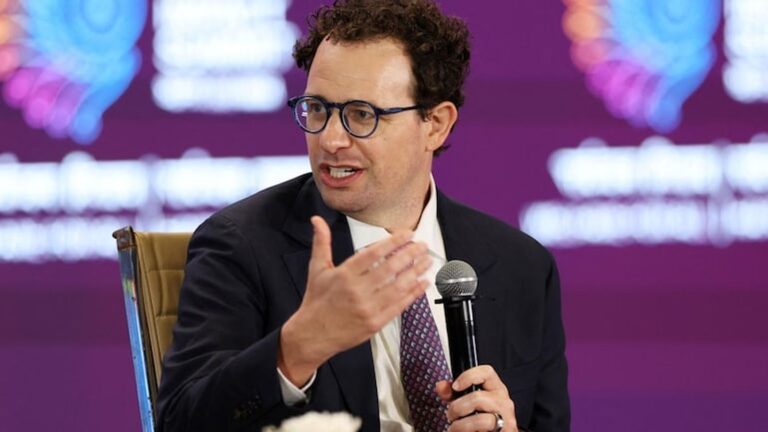 Anthropic CEO Dario Amodei wearing glasses and suit gesturing while speaking at a conference panel