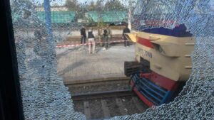 View through shattered glass showing a damaged train and investigators at Dnipro station after a dro