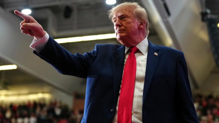 Donald Trump pointing and speaking at a political rally in a blue suit and red tie