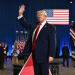 Donald Trump waving to supporters at a political rally with American flags