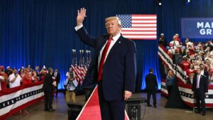 Donald Trump waving to supporters at a political rally with American flags