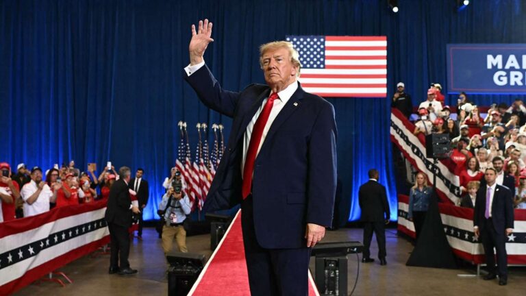 Donald Trump waving to supporters at a political rally with American flags