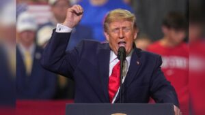 Donald Trump wearing a blue suit and red tie speaking at a podium