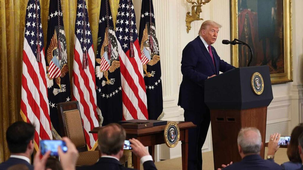 Donald Trump speaking at a podium in the White House with American flags behind him