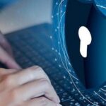 Close-up of hands typing on a laptop keyboard with a digital cybersecurity shield graphic overlay