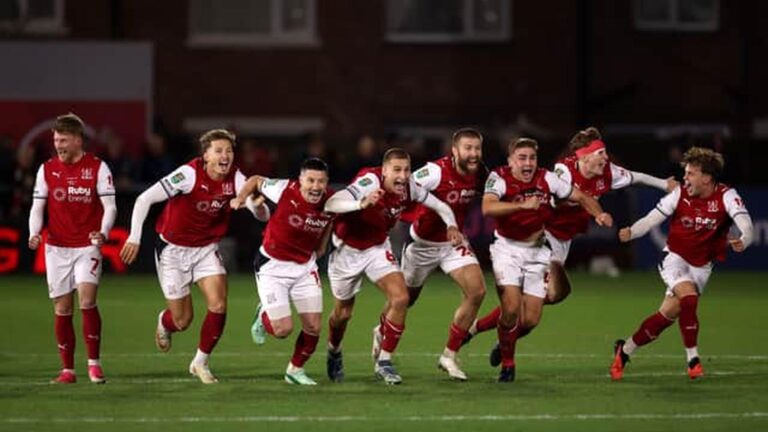 Fleetwood Town football players celebrating a goal on the pitch wearing red and white kits