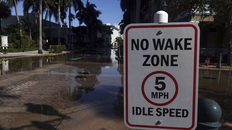 A no wake zone sign stands in front of a flooded residential street