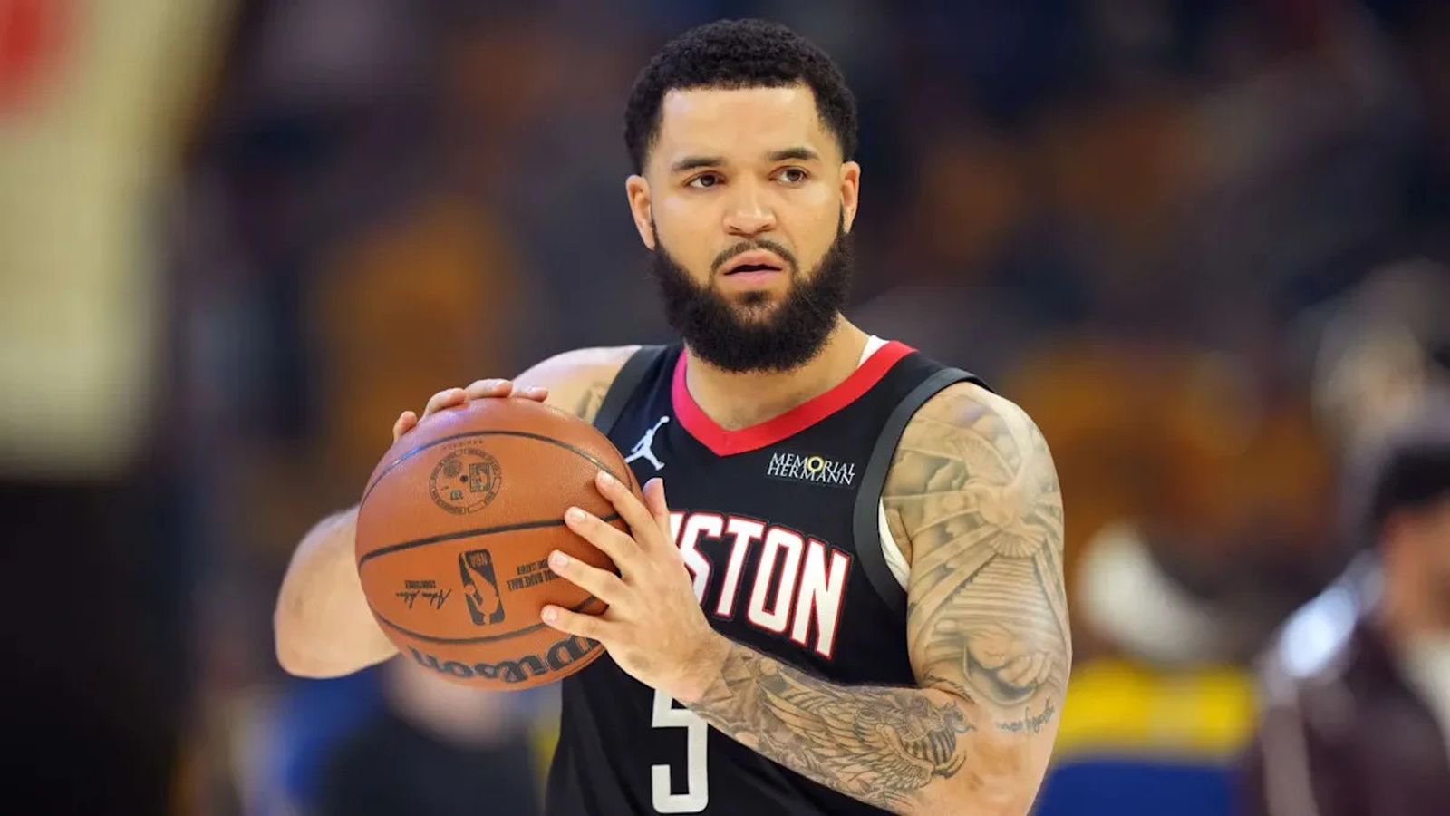 Fred VanVleet holding a basketball while wearing a black Houston Rockets jersey on the court