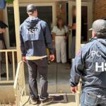 Federal HSI agents standing at a residential doorway talking to a resident during an investigation