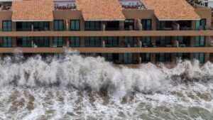 Large ocean waves crashing against a multistory coastal building during a storm
