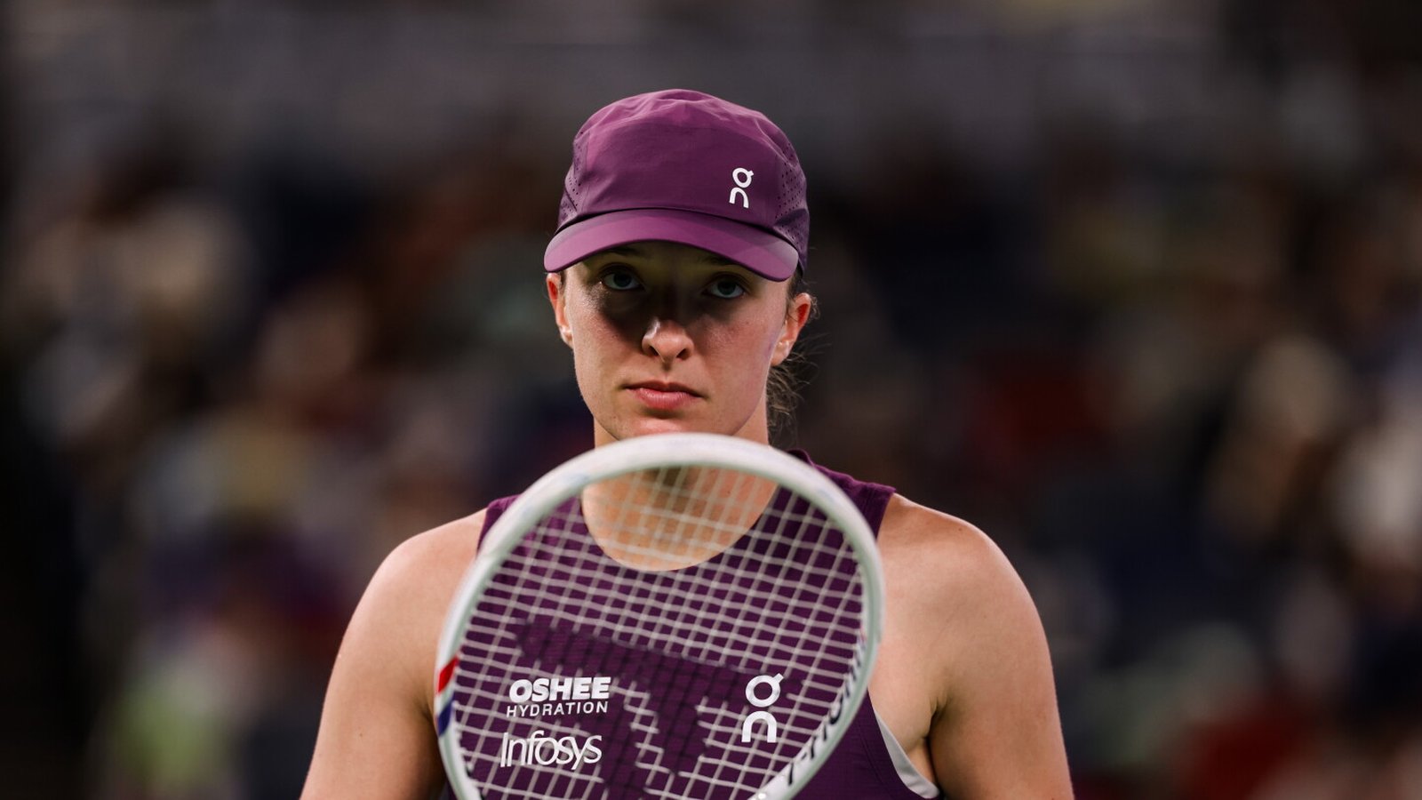 Tennis player Iga Swiatek holding her racquet and looking directly forward on court
