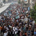 A large crowd of supporters carrying Pakistani flags participating in a long march toward Islamabad