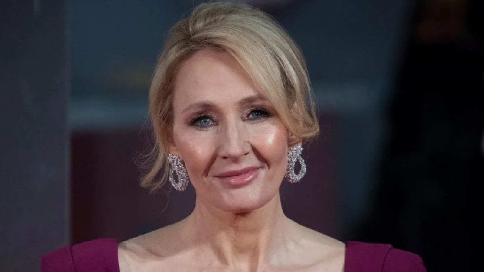 Close-up portrait of author J.K. Rowling wearing dangling earrings and a dark pink dress