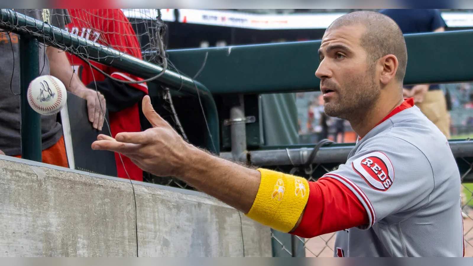 Joey Votto wearing a Cincinnati Reds uniform reaching out near the dugout