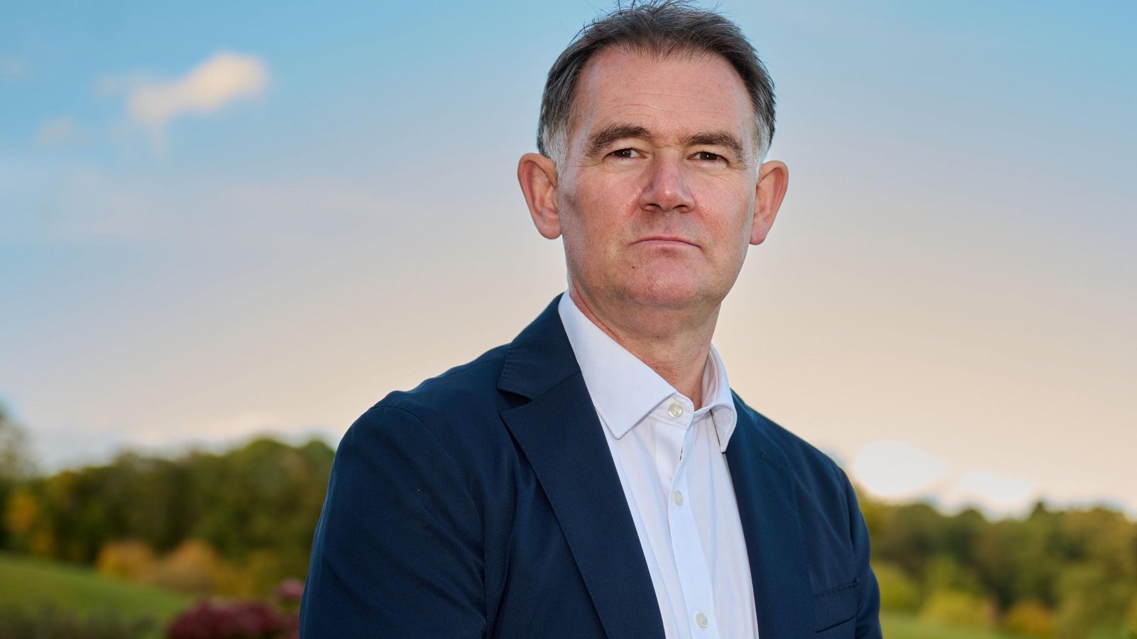 Portrait of John Murtough wearing a dark blazer and white shirt outdoors
